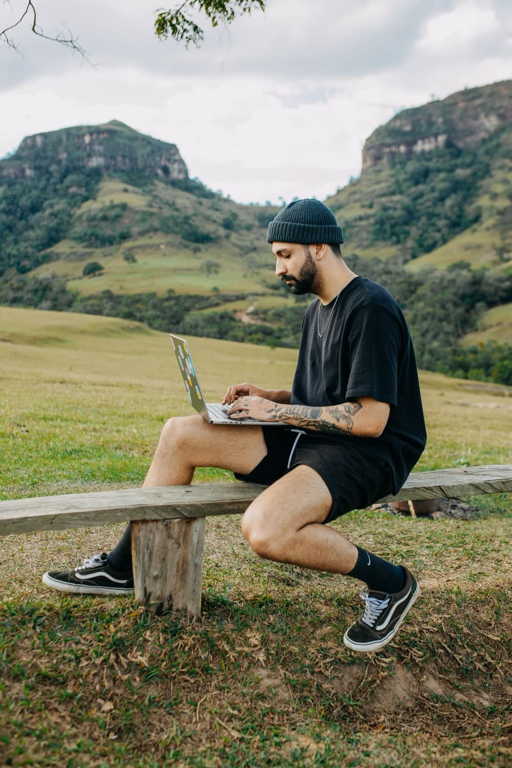 A man working on a laptop on a wooden bench in a green mountain valley