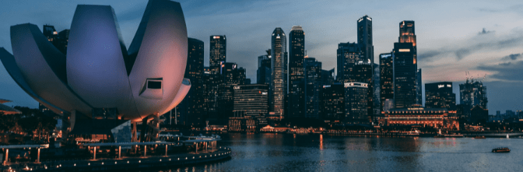 Singapore city skyline at dusk, featuring modern skyscrapers and the lotus-shaped ArtScience Museum reflected in Marina Bay