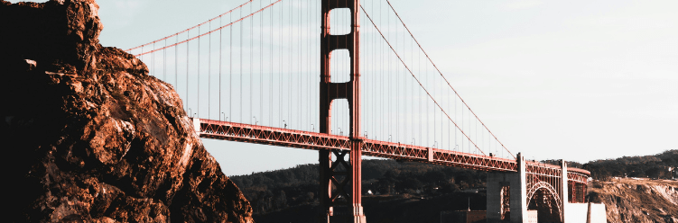 The Golden Gate Bridge spans across the water, connecting rocky terrain to distant hills under a clear sky