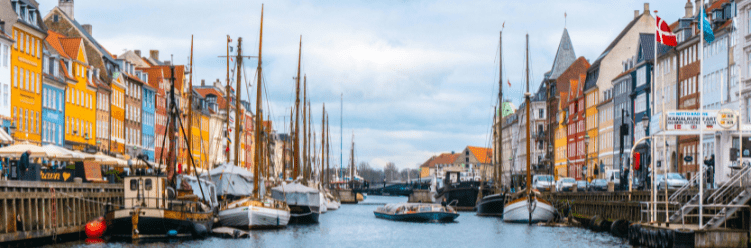 Colorful buildings and boats line both sides of a canal under a cloudy sky in an urban waterfront setting
