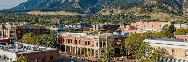 Downtown buildings with mountains and trees in the background on a clear, sunny day.