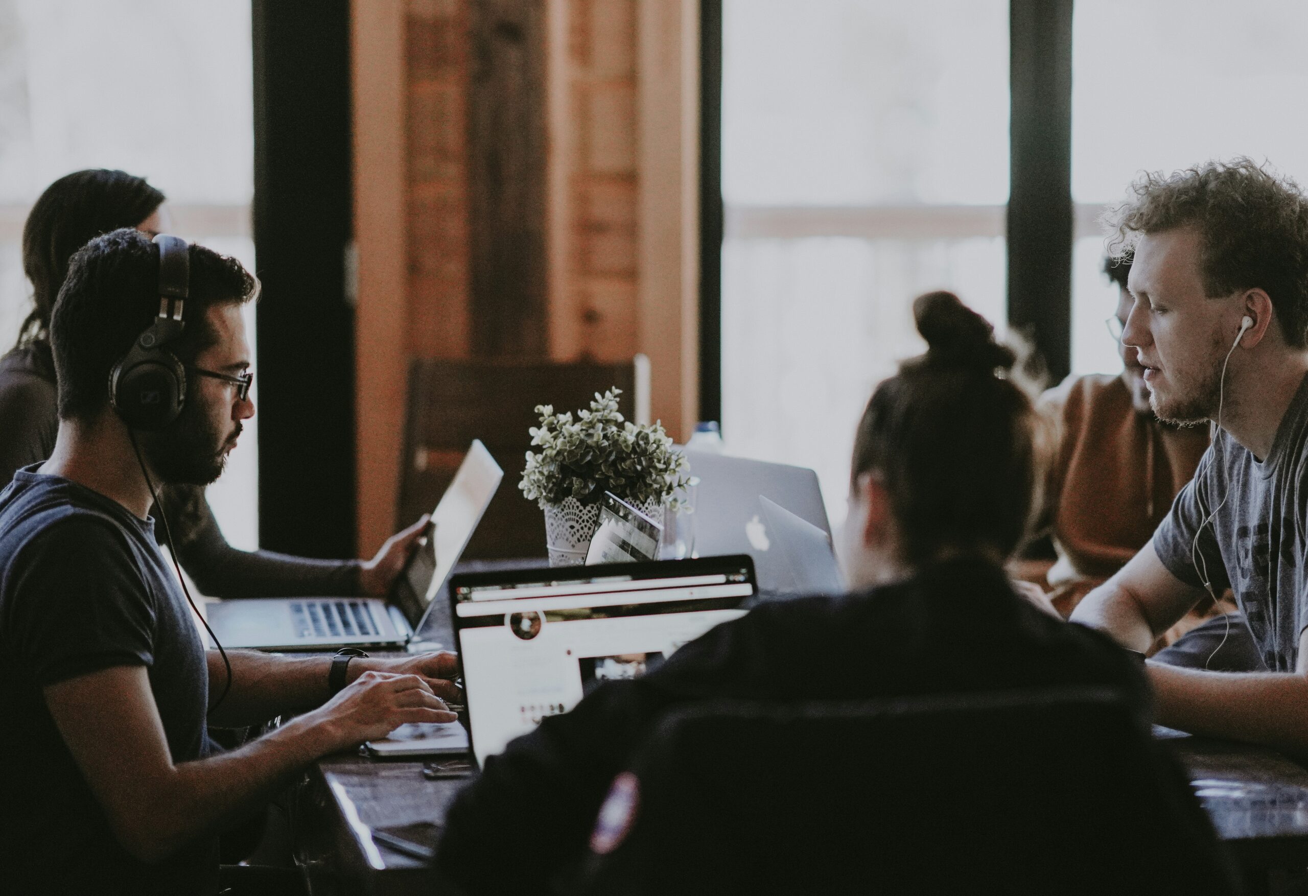 Four people working on laptops around a table in a modern, casual office setting.