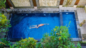 A person swims alone in a rectangular blue pool surrounded by plants and stone wall carvings.