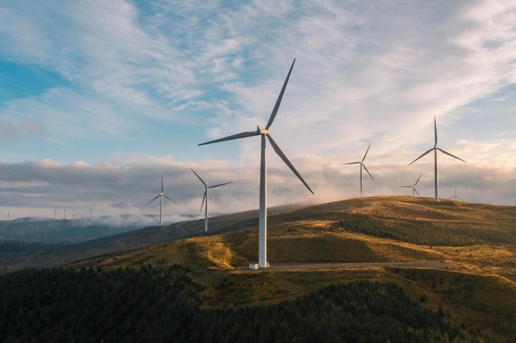 Wind turbines on grassy hills under a partly cloudy sky, generating renewable energy in a rural landscape.