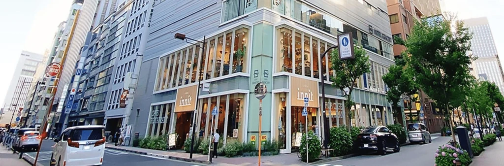 A modern two-story corner building with large windows, located on a city street lined with cars and trees.