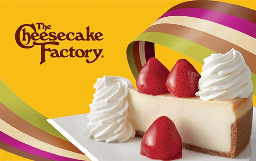 A slice of cheesecake with strawberries and whipped cream, The Cheesecake Factory logo in the background.