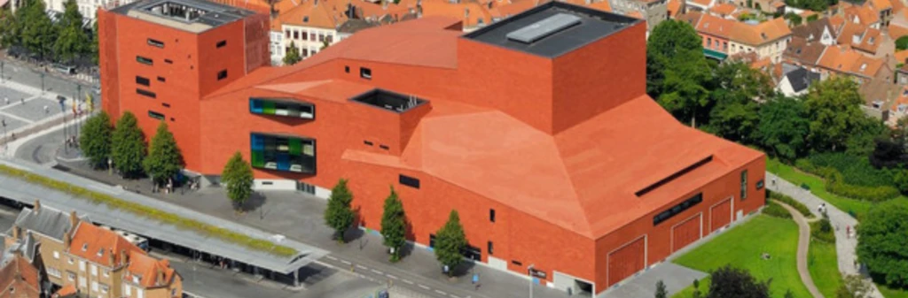 Aerial view of a large, modern red-brick building surrounded by trees and traditional houses.