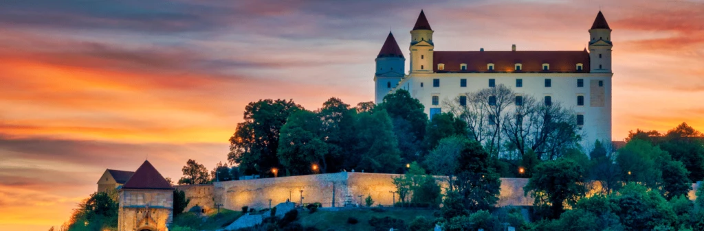 Bratislava Castle at sunset with vibrant clouds and trees in the foreground.