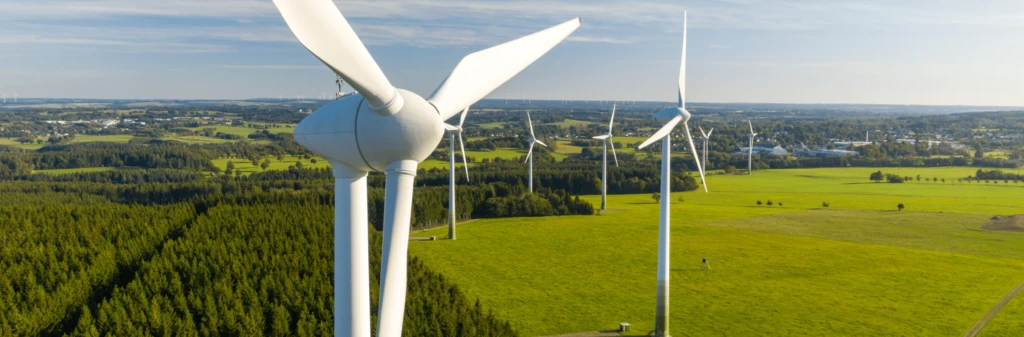 Close-up of wind turbines on a green landscape under a blue sky with scattered clouds.