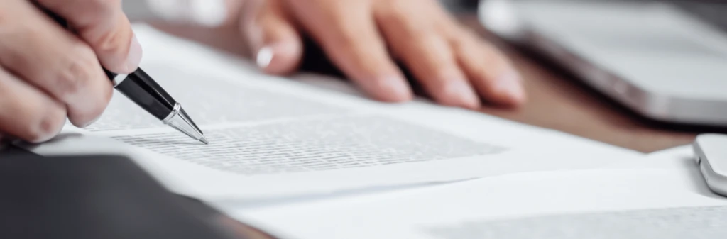 Close-up of a hand holding a pen and reviewing printed documents on a desk.