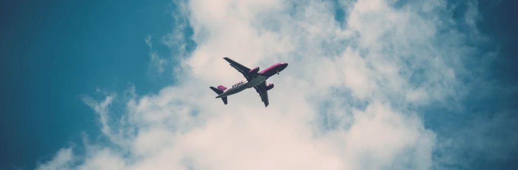 A commercial airplane flies overhead against a blue sky with scattered white clouds.
