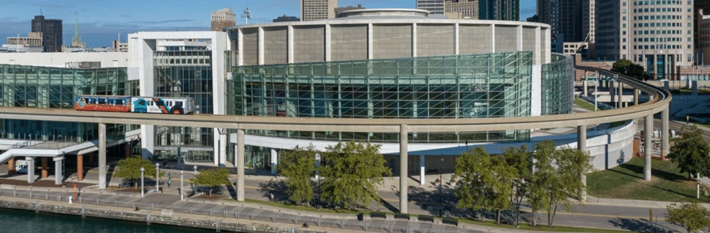 A modern glass and concrete building with a monorail passing in front, set in an urban waterfront area.