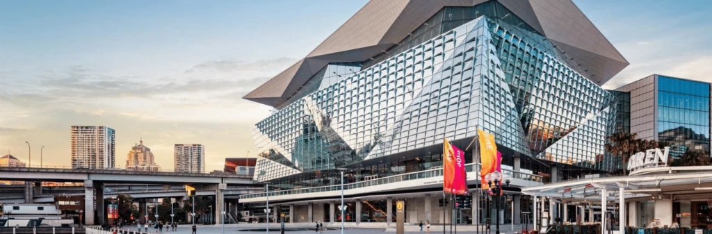 Modern glass building with colorful flags in front, set against a cityscape and blue sky.