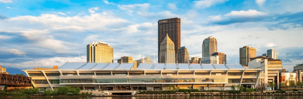 The David L. Lawrence Convention Center with Pittsburgh skyscrapers in the background under a blue sky.