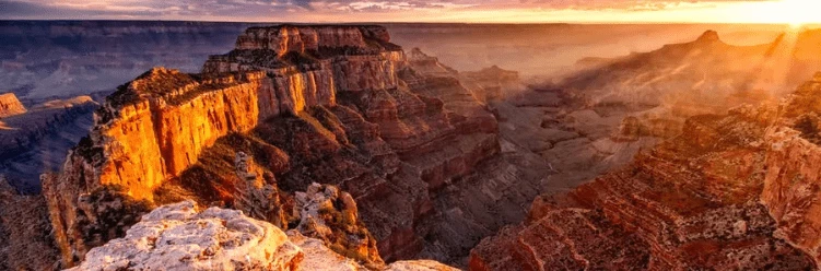 Sunrise over the Grand Canyon with golden light illuminating rugged cliffs and deep valleys.