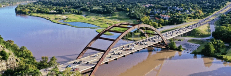 Aerial view of a busy arched bridge over a river surrounded by greenery and houses.