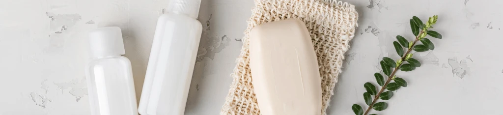 Two white bottles and a bar of soap rest on a textured mat beside a small green branch on a light gray surface, creating an ideal setting for presenting an Honest Company gift card.