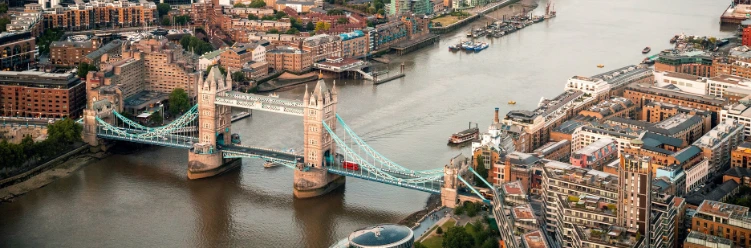 Aerial view of London’s Tower Bridge spanning the River Thames, with historic buildings and city streets surrounding the area.