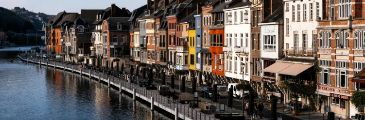 Charming riverside promenade in Dinant, Belgium, lined with colorful historic buildings and outdoor cafés beside the Meuse River.