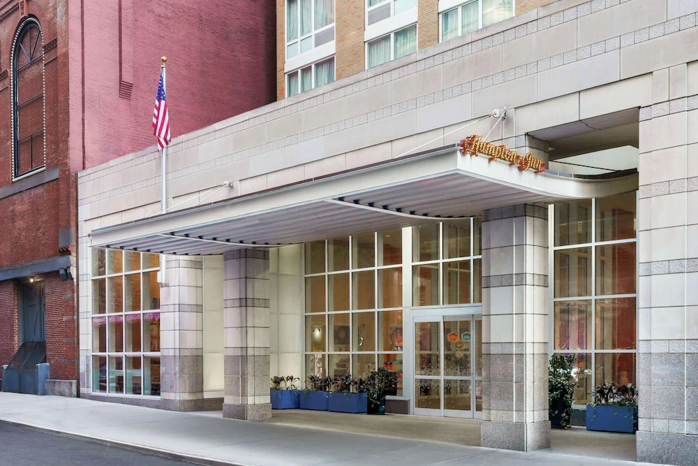 Hotel entrance with large windows, American flag, and Hampton Inn sign above the glass doors.