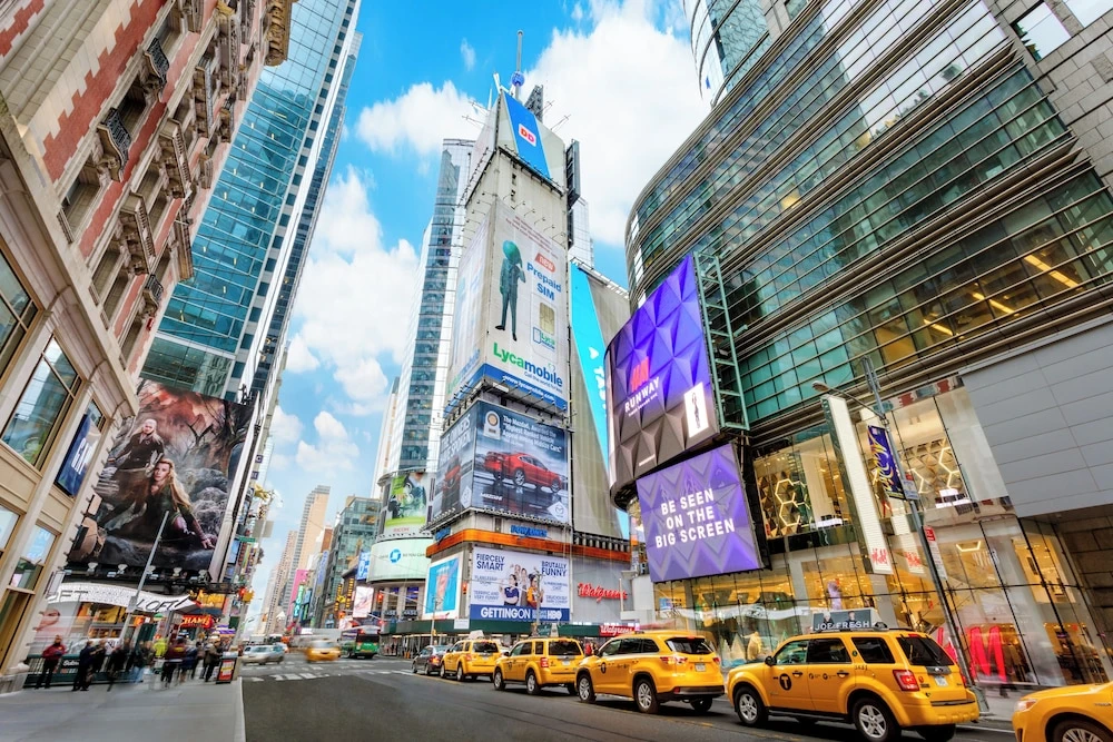 Times Square in New York City with tall buildings, digital billboards, and yellow taxis on the street.