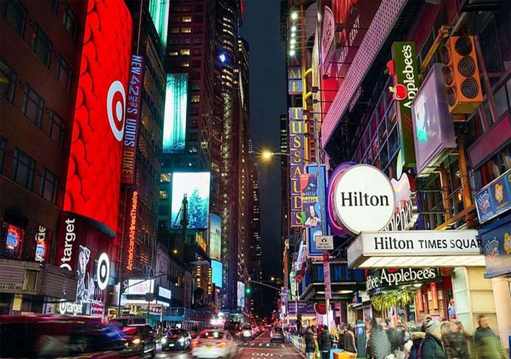 Times Square at night with bright billboards, hotel and restaurant signs, and busy street traffic.