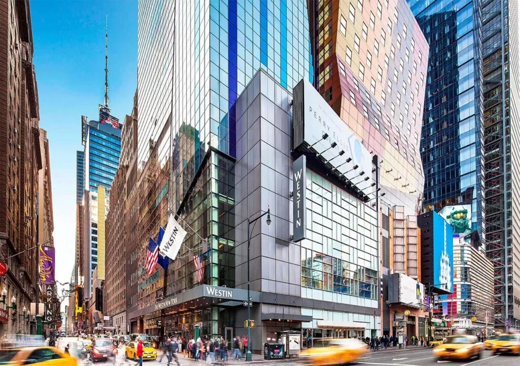 Busy city street with tall modern buildings, including The Westin hotel, and yellow taxis in motion.