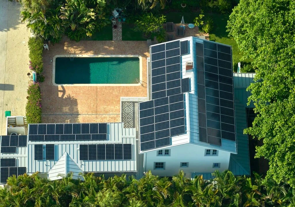 Aerial view of a house with solar panels on the roof and a swimming pool in the backyard.