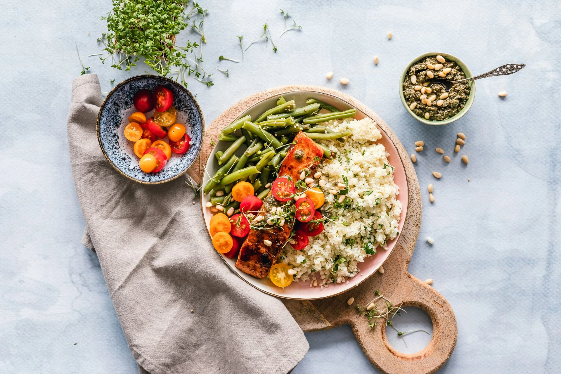 A plate with quinoa, green beans, salmon, and cherry tomatoes, next to a bowl of tomatoes and seeds.