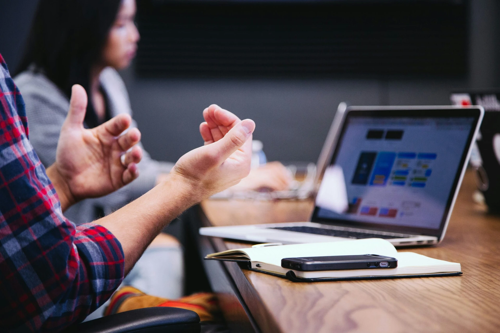 A person gesturing while discussing something near a laptop and notebook during a meeting.