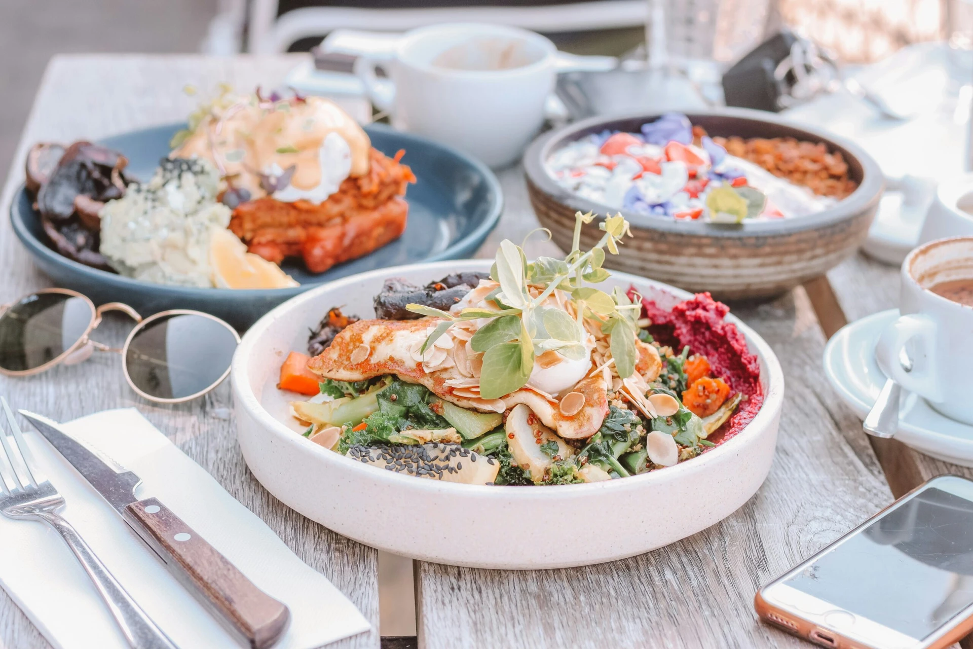 A table with plates of colorful brunch dishes, including eggs, vegetables, and yogurt, set outdoors.