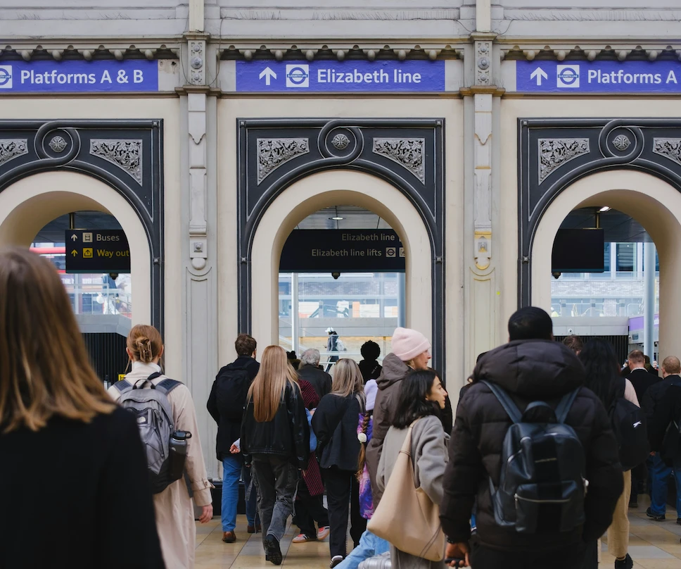 Commuters walk toward the Elizabeth line entrance at a busy train station.