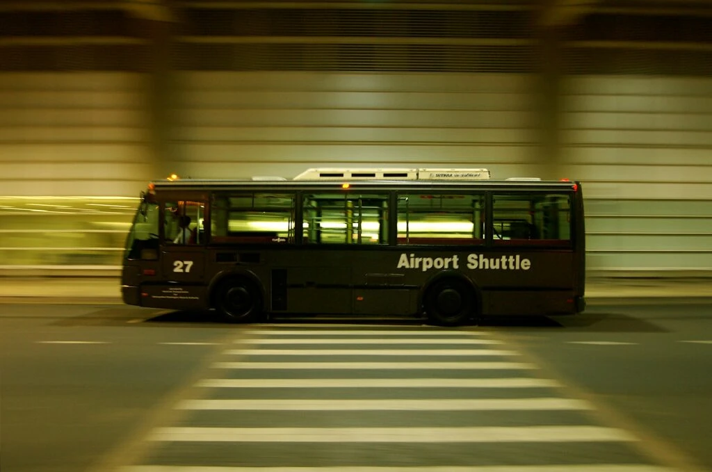 A moving airport shuttle bus passes a crosswalk in an urban setting at night.