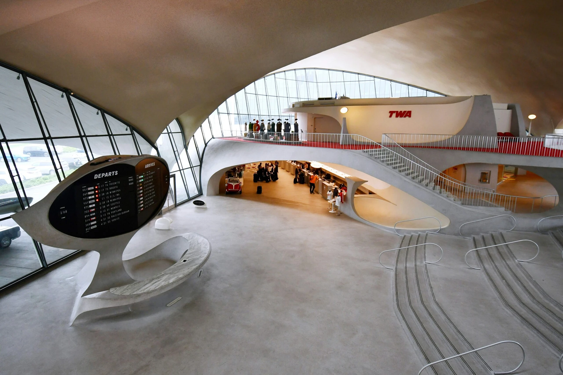 Mid-century modern airport terminal with curved architecture, a large departures board, and people at a check-in counter.