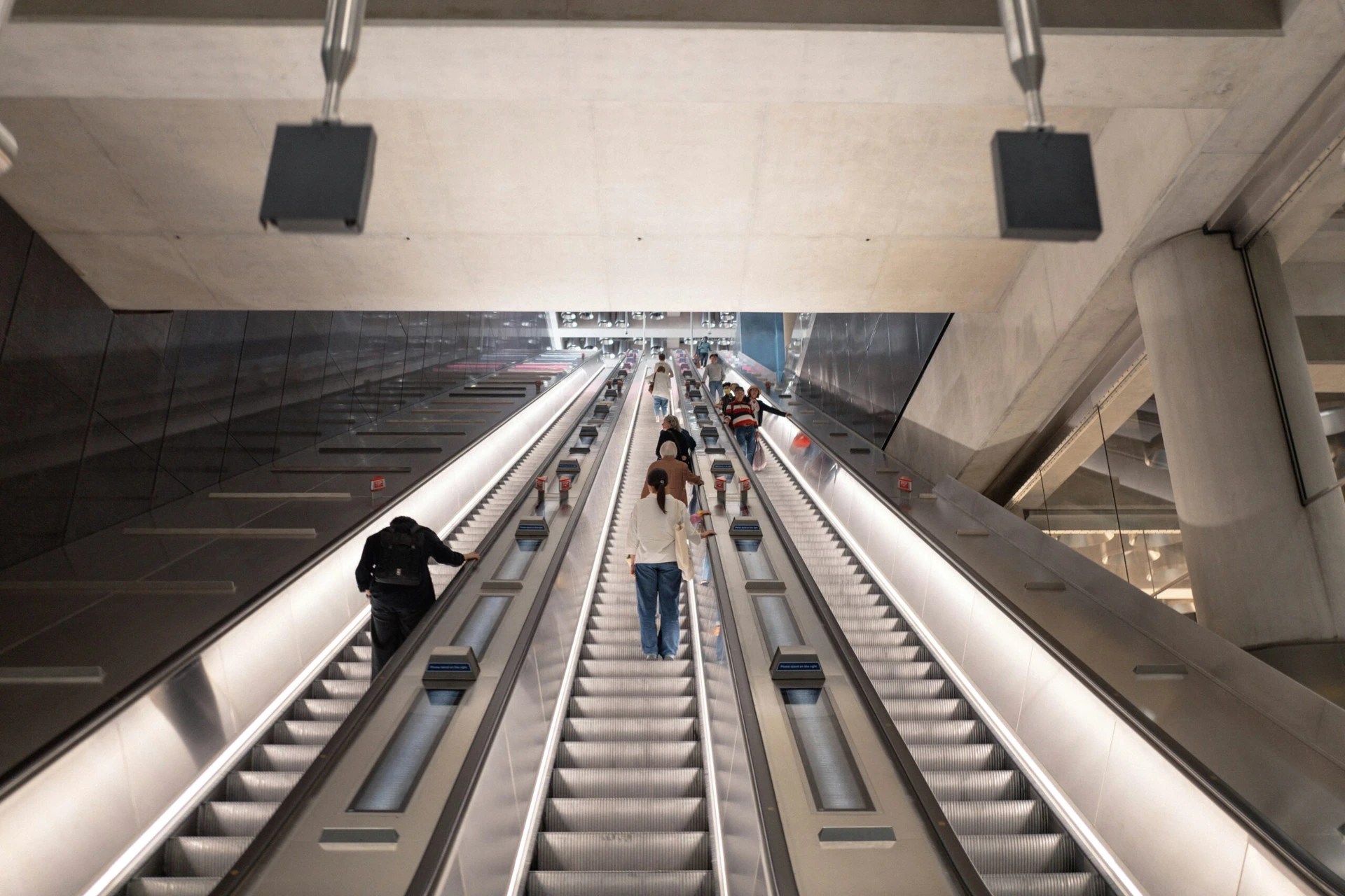 People ride up long, modern escalators in a large, spacious indoor public space.