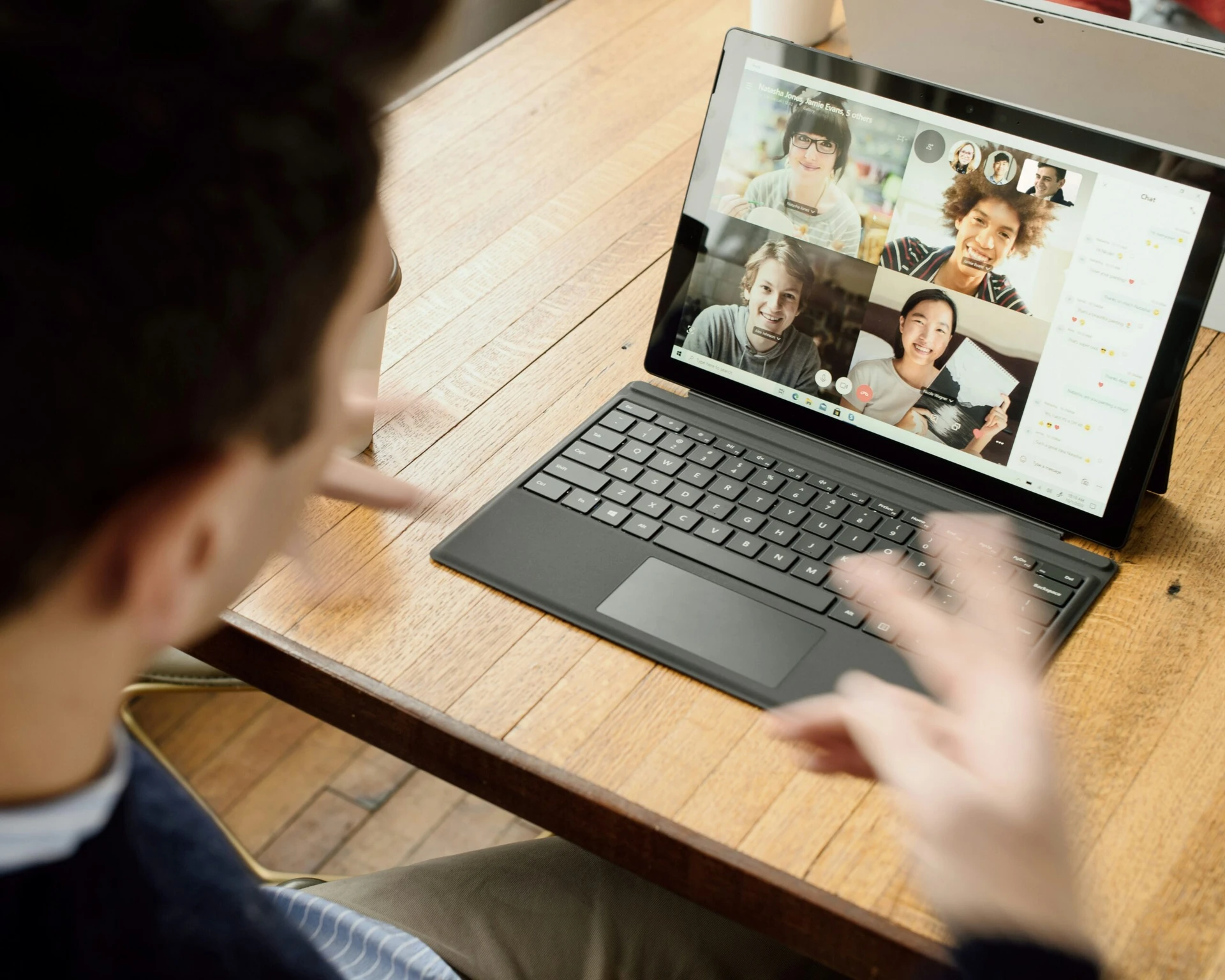 Person gesturing at a laptop screen during a video call with four people in a virtual meeting.