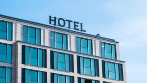 Modern hotel building with large blue windows and a HOTEL sign on the rooftop against a clear sky.