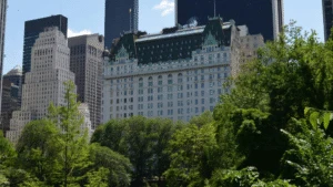 Historic white hotel with a green roof, surrounded by trees and modern skyscrapers in a cityscape.