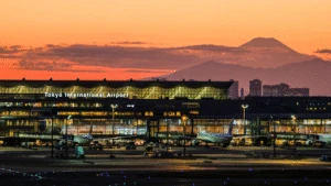 Tokyo International Airport at sunset, with Mount Fuji visible in the background and planes on the tarmac.
