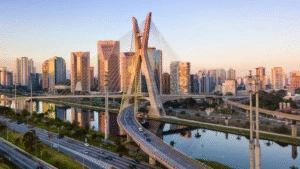 Cable-stayed bridge over a river, surrounded by city skyscrapers at sunset.