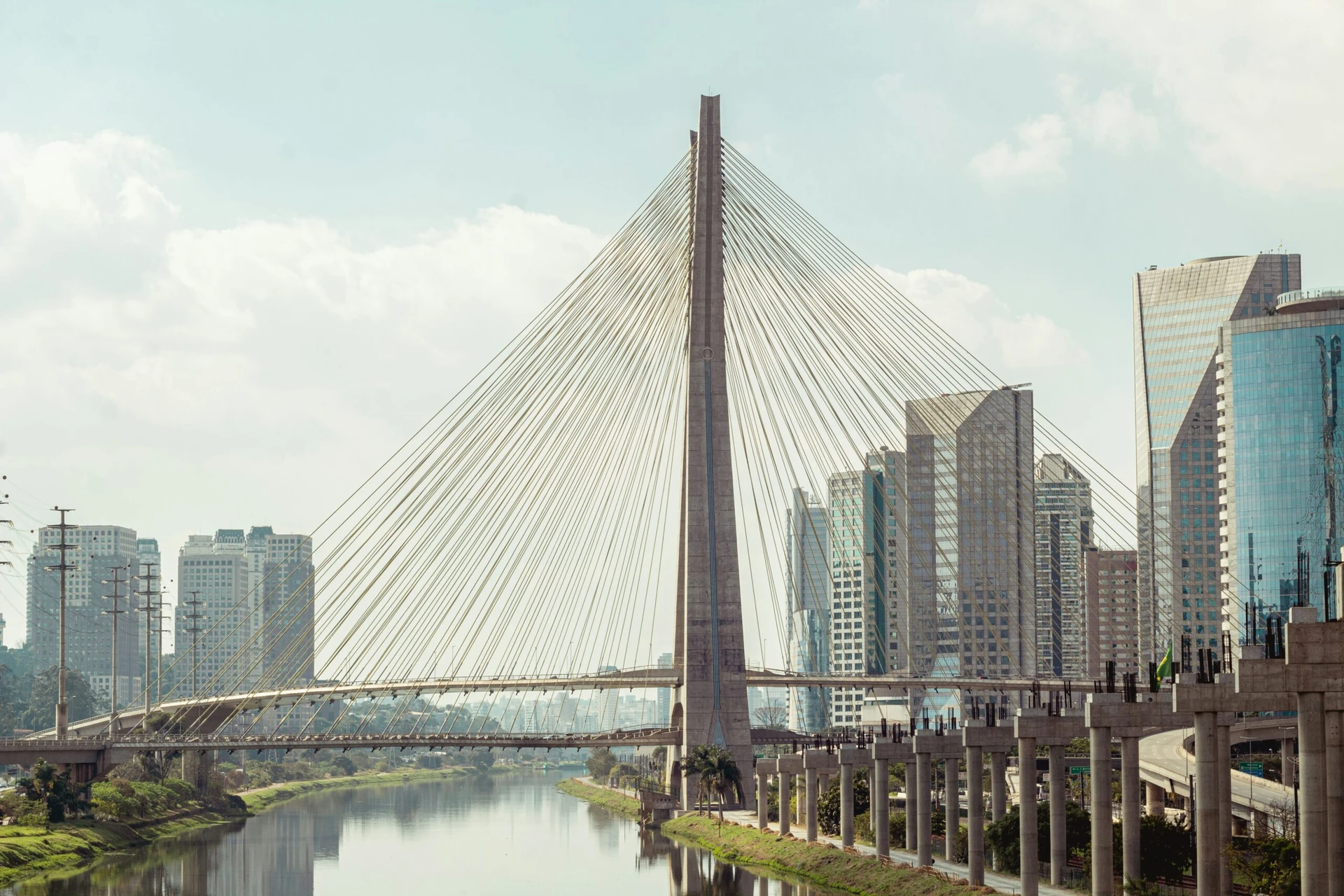 Cable-stayed bridge over a river with modern city buildings in the background on a clear day.
