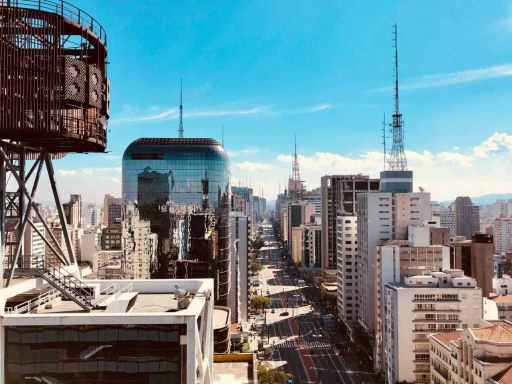 Cityscape with tall buildings, wide avenue, and communication towers under a clear blue sky.