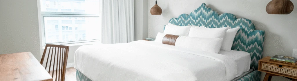 Modern bedroom with a large bed, patterned blue headboard, wooden desk and chair, and large window.