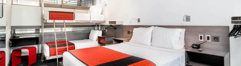 Modern hotel room with a double bed, bunk beds, and red-and-black bedding accents.