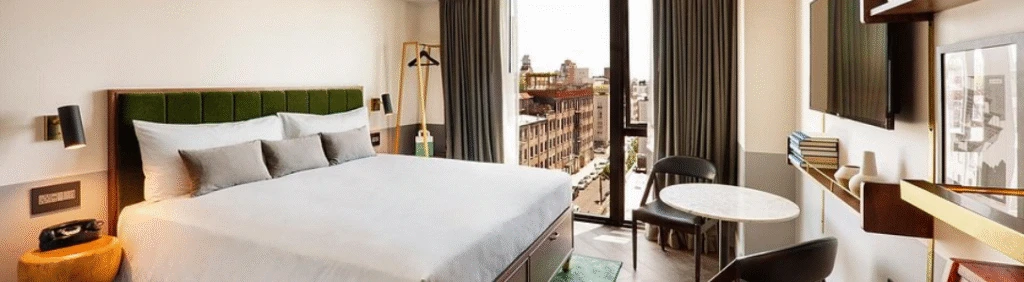 Modern hotel room with a large bed, seating area, and a window overlooking a cityscape.