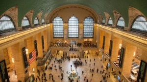 Aerial view of Grand Central Terminal’s main concourse with people, arched windows, and large American flag.