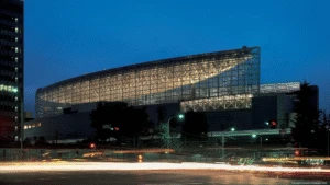 A modern glass building glows at night, with blurred car lights passing in the foreground.