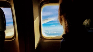 Person sitting by an airplane window looking out at blue sky and clouds above the wing.